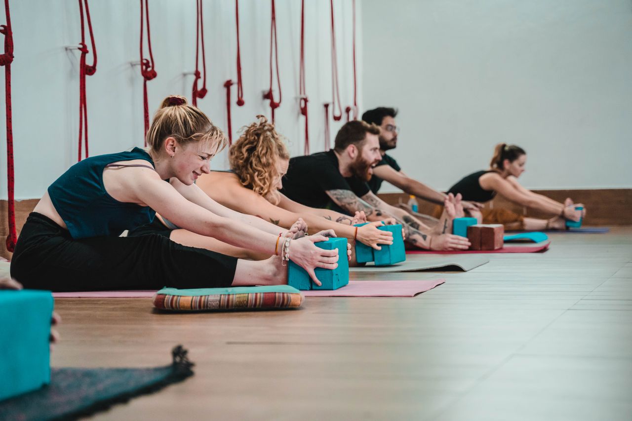 Services Individuals practicing yoga stretches using blocks in a Rishikesh studio.